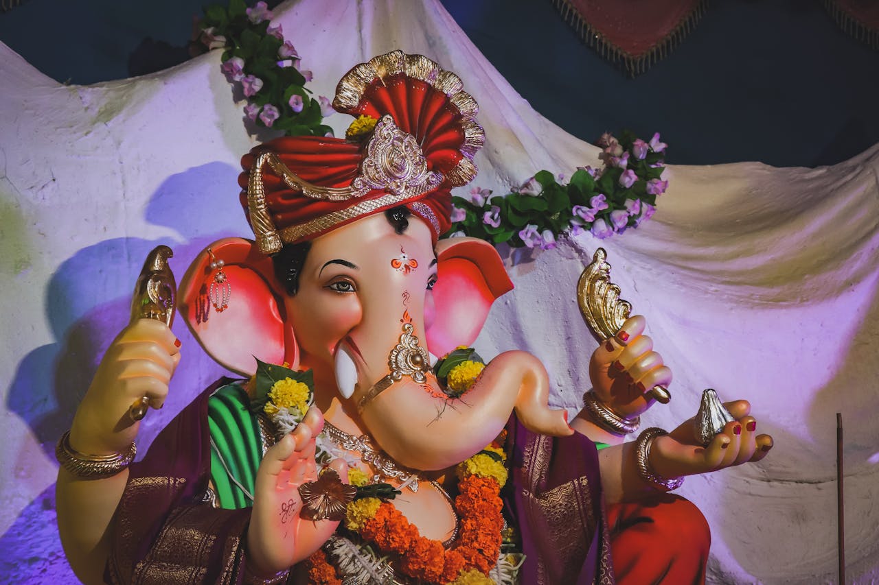 hero-img-01 Colorful Ganesha statue adorned with flowers and decor, symbolizing Hindu traditions.