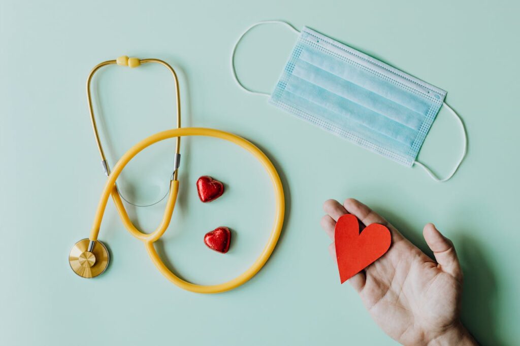 pexels photo 4386466 Top view of crop anonymous person hand with red paper heart on table with stethoscope and medical mask for coronavirus prevention